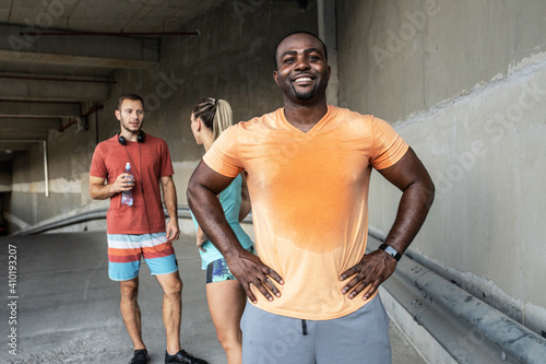 Young black man taking a break after jogging with his friends. He's standing against the wall and looking at the camera. Multi-ethnic group of people. 