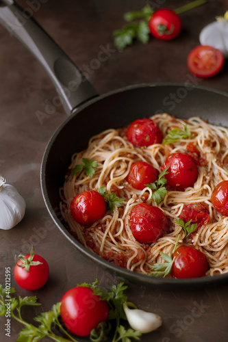 Pasta, spaghetti with tomato sauce and fresh parsley in a frying pan. Dark background.