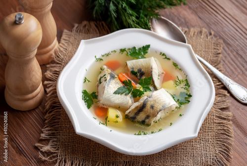 Ukha (Russian Fish Soup). White fish in a clear broth with diced root vegetable served in white plate on wooden table. Selective focus.