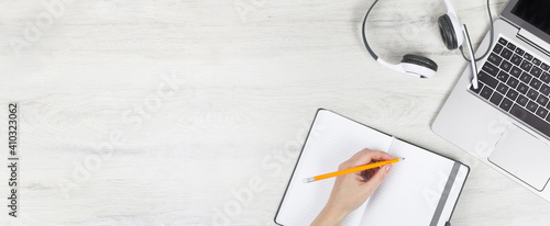 Laptop. keyboard and headphones on grey wooden desk. hand with pencil and notebook. Helpdesk or call center headset. Distant learning or working from home, online courses or support center concept.