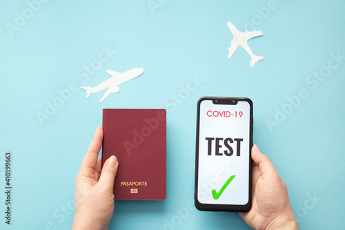 Person holding a passport with one hand and with the other a smartphone showing a copyright free negative test for coronavirus, on a blue background with white planes