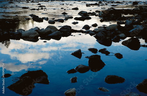 Reflection of clouds and sky on a river with stones