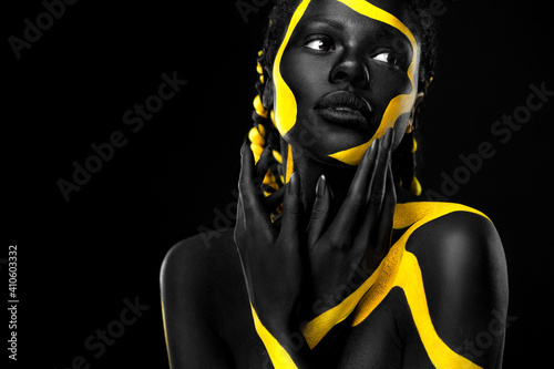 Yellow and black body paint. Woman with face art. Young girl with colorful bodypaint. An amazing afro american model with makeup.