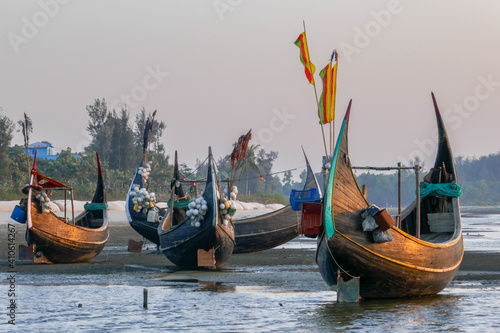 Landscape view of traditional wooden fishing boats known as moon boats glowing at sunset on beach near Cox's Bazar in southern Bangladesh