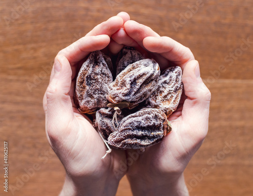 A bunch dried persimmons fruits in the hands on the wooden background. Horizontal frame, selective focus.