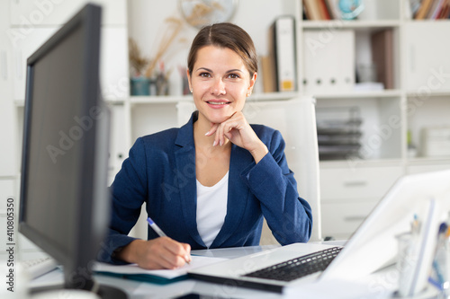 Portrait of successful busy female entrepreneur sitting at office desk with papers and laptop