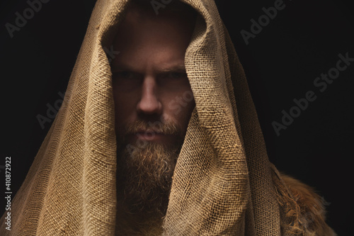 Portrait of a medieval bearded war monk dressed in animal skins and sacking. Low key. Focus on clothing. Atmospheric portrait of a character from an RPG