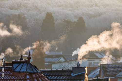 Rauchende Schornsteine über den Häuserdächern im Winter, angestrahlt von der Sonne