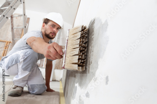 construction worker painter man with protective helmet, brush in hand restores and paint the wall, inside the building site of a house, closeup