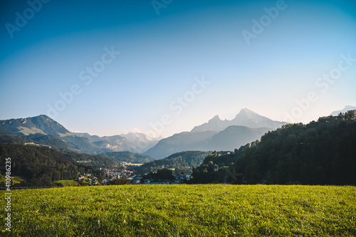 Amazing alpine mountain panorama with fresh green meadow in the front and the city of Berchtesgaden, Germany and the huge Watzmann mountain in the background under a clear blue sky.
