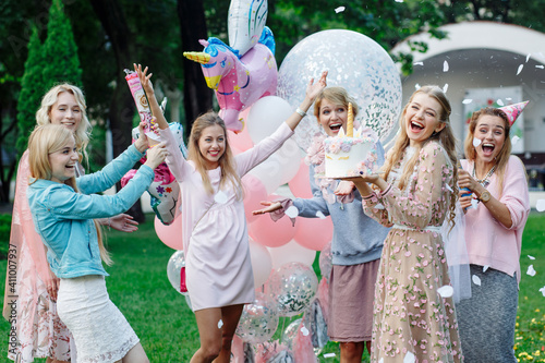 Six girls have fun at a birthday party in the park. They're wearing pink dresses and a bunch of pink balloons. They have cake and firecrackers