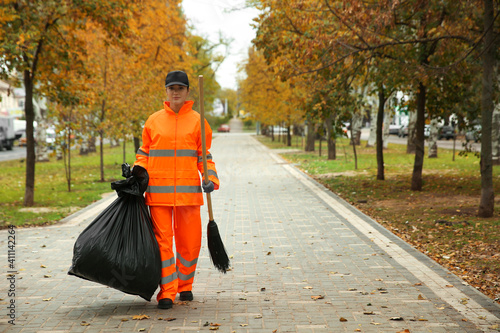 Street cleaner with broom and garbage bag outdoors on autumn day