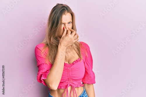 Beautiful caucasian woman wearing casual clothes smelling something stinky and disgusting, intolerable smell, holding breath with fingers on nose. bad smell