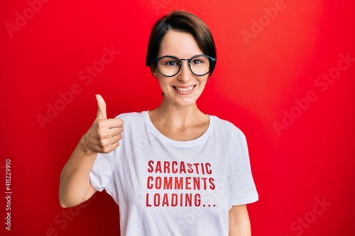 Young brunette woman with short hair wearing sarcastic comments loading t-shirt smiling happy and positive, thumb up doing excellent and approval sign