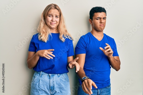 Young interracial couple wearing casual clothes disgusted expression, displeased and fearful doing disgust face because aversion reaction.