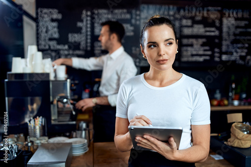 Female barista small business owner using digital tablet in cafe
