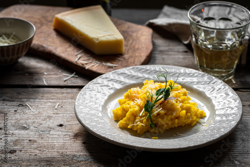 Rustic dinner with risotto all Milanese. Risotto with Saffron and parmesan on white plate on wooden table. 