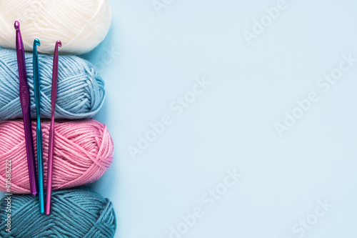 Multicolored crochet hooks with balls of yarn on a blue background with copy space.