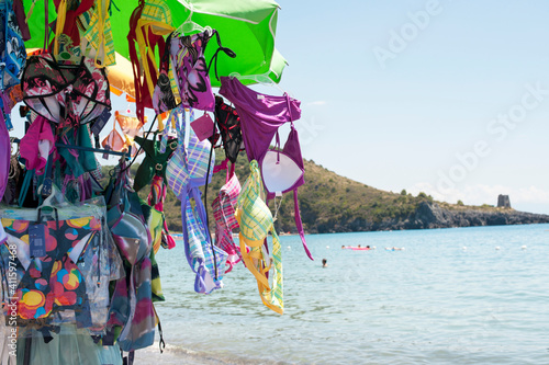 Hawker selling swimsuits on the beach roaming around with a stall. 