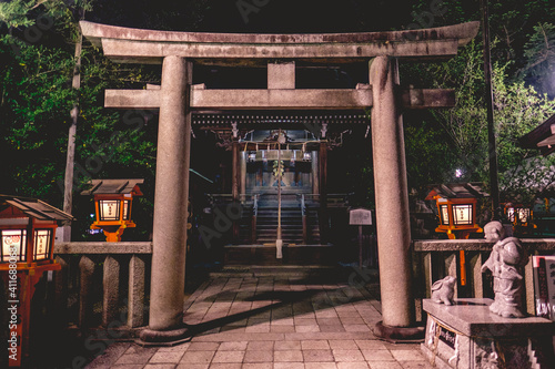 Girl and rabbit statue, stone torii gate and little shinto altar with bell and wooden lamps at Yasaka shrine in night, Kyoto, Japan