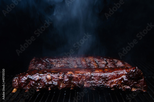 Hot babyback ribs cooking on a pellet smoker grill with caramelized barbecue sauce slathered on top. 