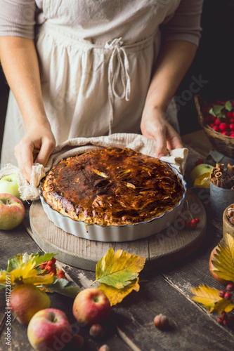 Homemade apple pie surrounded by fresh fruits, nuts, apples in woman hands