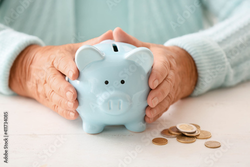 Senior woman with piggy bank at table. Concept of pension