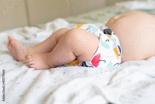 A baby lying on a bed with the focus on the baby's legs and cloth diaper with a pretty umbrella print