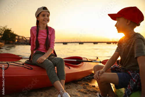 Happy children sitting on kayaks near river at sunset. Summer camp