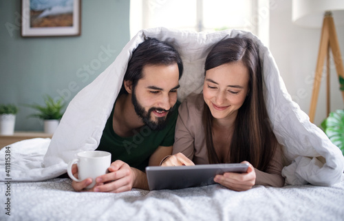 Young couple in love using tablet on bed indoors at home.