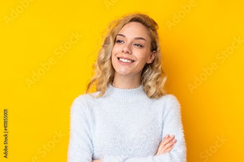 Young blonde woman isolated on yellow background looking up while smiling
