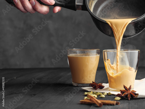 Hot masala tea is poured into a glass glass. Steam comes out of the mug. Gray background. Copy space.