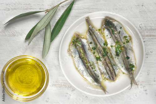 Pickled anchovies or sardines fillet in oil with herbs and olive branch for tapas or antipasti on the white wooden background