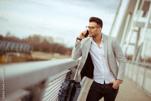 Young businessman talking on cell phone on the bridge. Satisfied yuppie smiling and enjoying outdoors