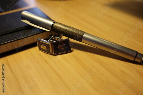 inkpen and cuff-links on wooden table with notebook, home office