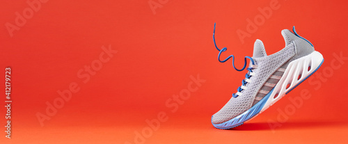 Fashion stylish sneakers with flying laces. Running sports shoes on orange background.