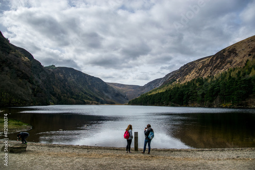 Dos jóvenes observan un lago entre colinas y con nubes que amenazan lluvia.