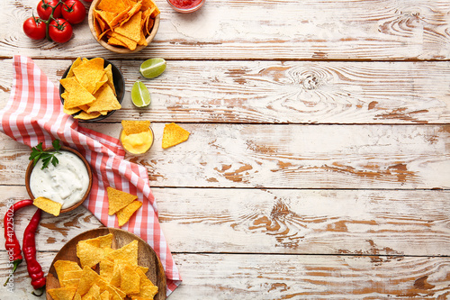 Plates with tasty nachos and sauces on light wooden background