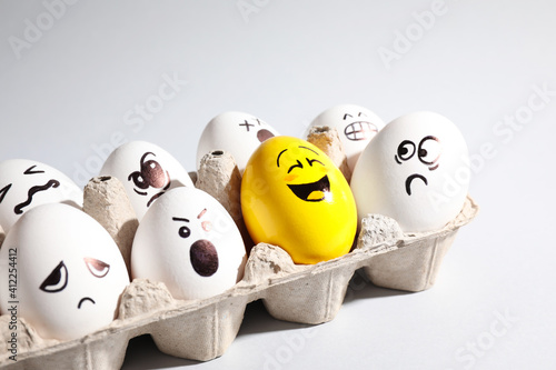 Yellow smiley egg among others with negative emotions in package on light background