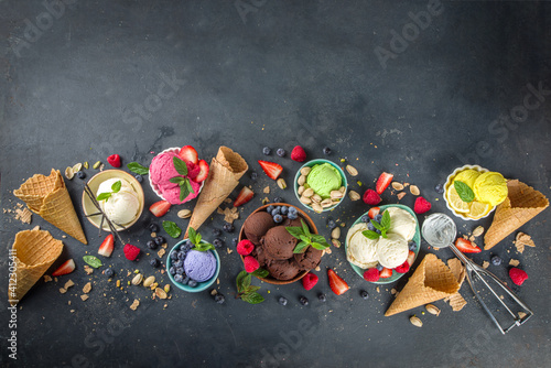  Various colorful ice cream balls in different bowls, with ice cream waffles cones and flavor ingredients - pistachio nuts, berries, lemon, chocolates, vanilla beans, mint. Dark background copy space 