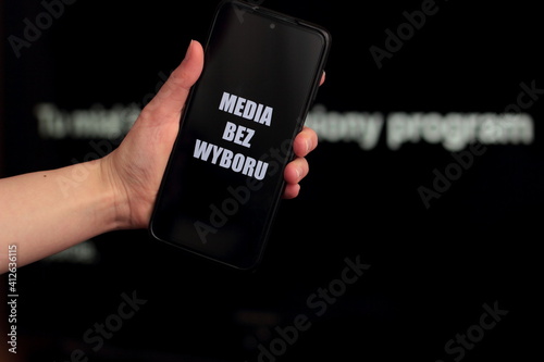 Media blackout protest in Poland. A person is holding a smartphone with the sign “Media bez wyboru” (Eng. Media without a choice) in front of a black TV screen.