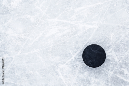 Black old rubber puck on ice background. Closeup. Empty place for text. Top down view.