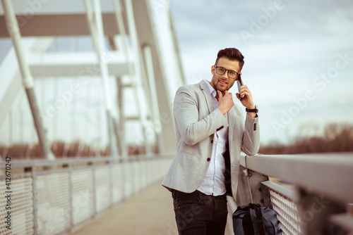 Young businessman talking on cell phone on the bridge. Satisfied yuppie smiling and enjoying outdoors