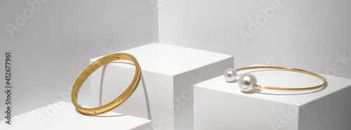 Panoramic shot of Two golden bracelets on white geometric background