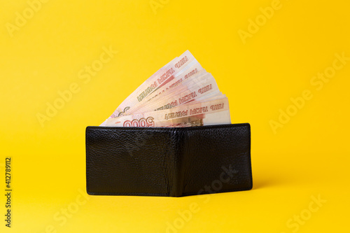 Economic prosperity. Black leather wallet opened, filled with a fan of five thousand rubles. Yellow background. Copy space