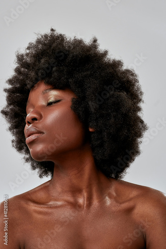 Portrait of african american female model with afro hair and perfect smooth glowing skin looking down, posing isolated over gray background