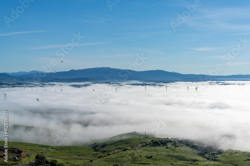 view of rolling hills landscape in Andalusia with many wind turbines above the fog in the valleys and blue sky above