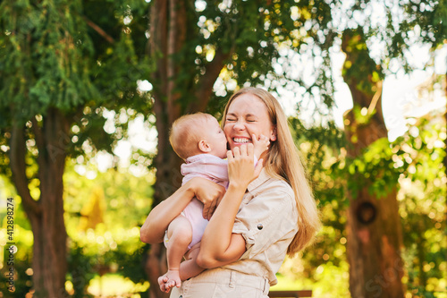 Adorable baby kissing her mom, young happy laughing mother in summer park