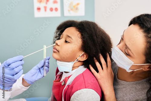 African American little girl with her mother during PCR test of COVID-19 in a medical lab. Physician taking a nasal swab for coronavirus sample