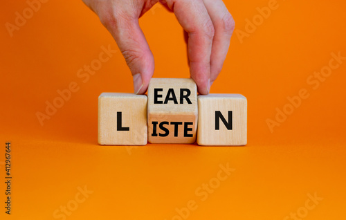 Listen and learn symbol. Businessman turns a wooden cube and changes the word 'listen' to 'learn'. Beautiful orange background, copy space. Business, education and listen and learn concept.